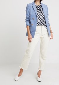 Blazer de lino azul con botones marrones, blusa de rayas en blanco y negro, jeans blancos con dobladillo deshilachado y zapatillas blancas sin cordones.