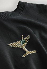 Sort crewneck sweatshirt med et perlesyet cocktailglasdesign i guld, sølv og grøn, der fremhæver detaljerigdom og tekstur.