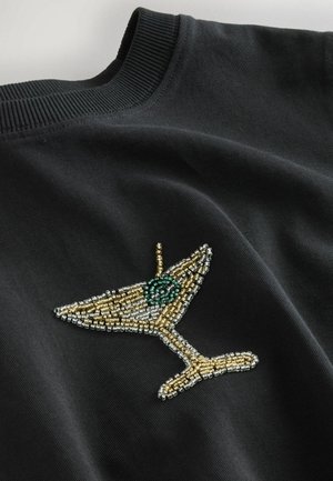 Černá mikina s kulatým výstřihem, která zobrazuje design koktejlové sklenice zdobené korálky v zlaté, stříbrné a zelené barvě, s nádhernými detaily a texturou.