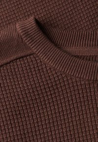 Gros plan d'un pull marron en maille montrant un col côtelé et un motif gaufré texturé sur le tissu.