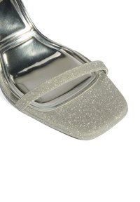 Open-toe sandaal van zilveren glitters. Heeft een vierkante neus en twee slanke bandjes. Glanzende metalen binnenzool en strakke ontwerpelementen.
