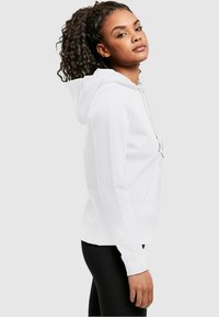 Fehér kapucnis pulóver puha anyagból, elülső zsebből, húzózsinórral ellátott kapucnival és bordás mandzsettával. Slim fit fazon sima textúrával.
