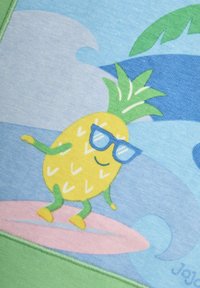 Geltona ananaso karikatūra su žaliomis galūnėmis, nešiojanti mėlynus akinius, sėdinti ant rožinės lentos prieš mėlyną bangų foną.