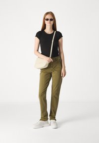 Juodas trumpas rankovės marškinėliai, alyvuogių spalvos kelnės ir baltos sportbačiai. Šviesiai ruda per petį nešama kuprinė su uždengta dalimi. Modelis dėvi tamsius akinius nuo saulės.