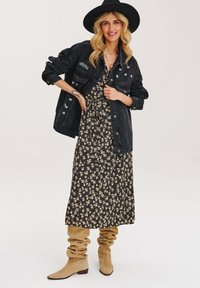 Čierna džínová bunda s vyšívanými detailmi, kombinovaná s maxi šaty s kvetinovým vzorom v čiernej a žltej farbe. Semišové voľné béžové čižmy.