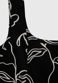 Svart tyg med ett vitt blommönster, med breda axelband och en texturerad yta, som framhäver den sömlösa integrationen av design och material.