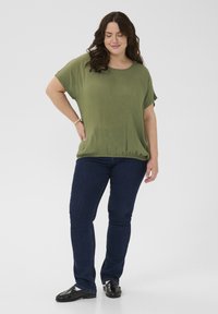 Top suelto verde oliva con mangas cortas y dobladillo fruncido, combinado con jeans azul oscuro y mocasines negros. Textura suave.
