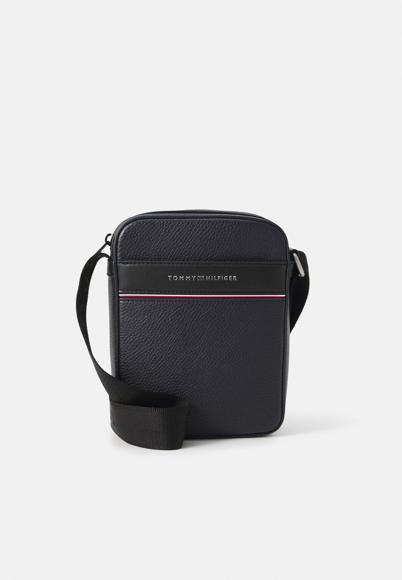 Navy leather crossbody bag with a textured surface, featuring a black accent with logo and a multi-colored stripe. Adjustable strap included.