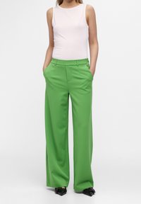 Pantalones anchos verdes con un acabado texturizado, que cuentan con bolsillos frontales y una cinturilla ajustada. Combinados con una blusa sin mangas blanca ceñida.