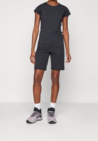 Czarna koszulka na krótki rękaw zestawiona z czarnymi szortami cargo, uzupełniona jasnofioletowymi butami do wędrówki i białymi skarpetkami sięgającymi do kostek. Prosty design.