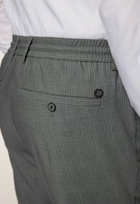 Graue Nadelstreifenhose mit elastischem Bund, ausgestattet mit einer Gesäßtasche mit einem schwarzen Knopf und einem kleinen Markenlogo-Patch.