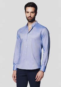 Jasnoniebieska koszula z długim rękawem, wykonana z gładkiego materiału, z kołnierzykiem typu band, z zapięciem na guziki z przodu i kontrastującymi niebieskimi mankietami.