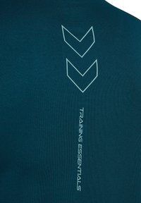 Donkerblauwe trainingshirt met textuur, omhoog wijzende chevrons en de tekst "TRAINING ESSENTIALS" aan de zijkant in lichtblauw.