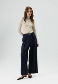 Beige coltrui, marineblauwe wijde broek met plooien, zwarte riem en bruine schoenen met hak. Eenvoudig, modern ontwerp en gladde textuur.