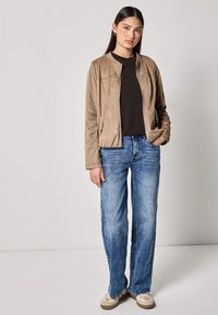 Giacca bomber in suede beige con zip e tasche laterali, abbinata a jeans a gamba larga di un blu chiaro e scarpe beige. Design semplice e casual.