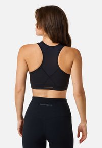 Black athletic sports bra with a racerback design, smooth texture, and reinforcement seams; brand logo displayed at the back.