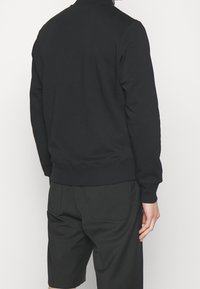 Sweat-shirt noir avec un design simple, col et poignets côtelés, fait d'un matériau doux, associé à un short noir.