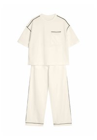 Dwuczęściowy zestaw w off-white z bawełny. Krótki rękaw bluzki z kieszonką na piersi i czarnym wykończeniem, w zestawie z luźnymi spodniami z bocznymi paskami.