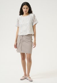 White lace cropped top with short sleeves, paired with a beige denim skirt featuring a tie waist and side snap accents.