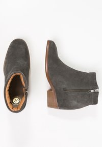 Graue Wildleder-Ankle-Boots mit einem hellbraunen Innenfutter, einem seitlichen Reißverschluss und einem kleinen braunen Blockabsatz. Glatte Textur und runde Zehenform.