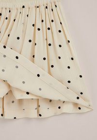 Jupe en tissu couleur crème avec des pois noirs et une partie pliée visible montrant l'envers du matériau.