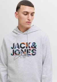 Sudadera gris claro con un vibrante estampado de logo que incluye letras en varios colores y patrones, cordones y un acabado de tejido texturizado.