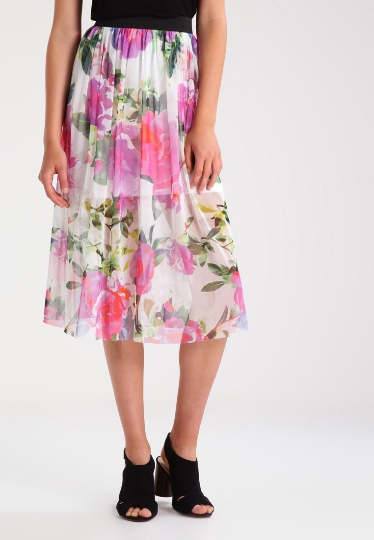 Jupe midi florale en tissu léger et transparent, avec des motifs roses, rouges et verts, taille élastique et chaussures à talons ouverts noires.