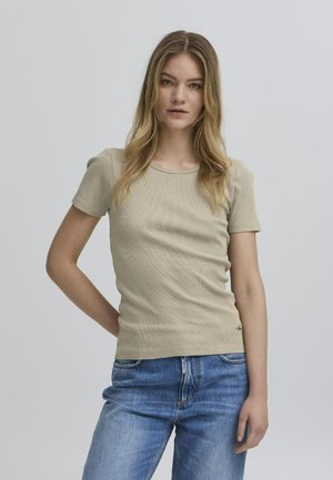 Beige csíkos rövid ujjú póló kerek nyakkal. Kék farmernadrággal viselve, amelynek alján egy diszkrét logó részlet található.