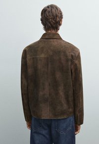 Giacca in suède marrone con colletto classico, dettagli di cucitura visibili e vestibilità rilassata, vista da dietro.