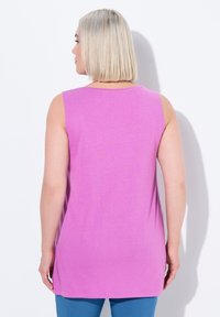 Ärmelloses pinkes Oberteil aus weichem Stoff, mit lässiger Passform und Rundhalsausschnitt, getragen mit türkisfarbenen Hosen.