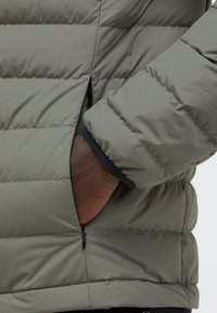 Olive green puffer jacket with horizontal quilted design, zippered side pockets, and a textured finish. Featuring a black inner lining.