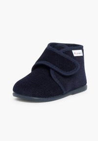 Chausson tout-petit bleu marine en tissu côtelé, bride ajustable à scratch, semelle souple et petite étiquette de marque colorée sur le côté de la cheville.