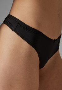 Zwarte bikini-stijl onderbroek van gladde stof, met een kanten rand langs de tailleband en een klein strikje aan de achterkant.