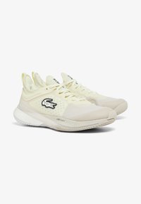 Scarpe sportive color beige chiaro con tomaia in rete e colletto imbottito. Presentano un logo nero e una suola strutturata per aderenza e supporto.