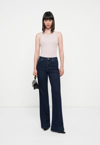 Un top fără mâneci de culoare roz deschis, asociat cu blugi evazați de culoare albastru închis cu talie înaltă. Blugii au un design clasic cu cinci buzunare și cu falduri.