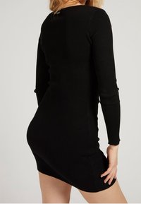 Robe noire côtelée à manches longues avec une silhouette ajustée, dotée d'un col rond et d'une texture lisse.