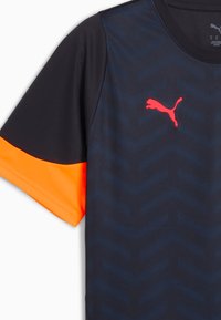 Koszulka sportowa Puma z ciemnoniebieskim korpusem, pomarańczowymi akcentami na rękawach i teksturowanym wzorem w zygzak. Posiada okrągły dekolt i logo.