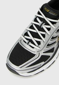 Black and silver Skechers sports shoe with white laces, breathable mesh upper, and thick cushioned sole, close-up view.