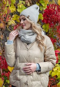 Doudoune beige avec boutons, écharpe en tricot texturé beige et bonnet assorti. Décoré de feuillages d'automne aux couleurs vibrantes.