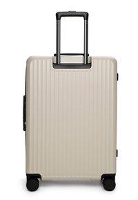Beige harde koffer met verticale ribbels, zwarte handvatten, telescopisch handvat uitgeschoven, en vier zwarte draaibare wielen.