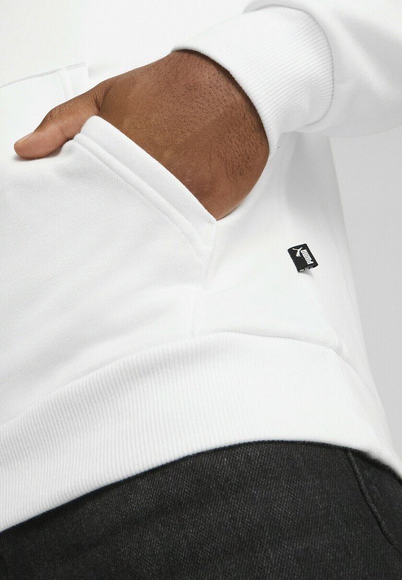 Sudadera blanca con ribetes en el dobladillo y los puños, que cuenta con un bolsillo lateral y una pequeña etiqueta de logo negra. Textura suave y diseño relajado.