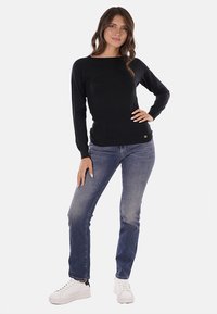 Maglione nero a maniche lunghe con scollo tondo, abbinato a jeans di denim blu e sneakers bianche. L'outfit presenta un delicato dettaglio con logo.