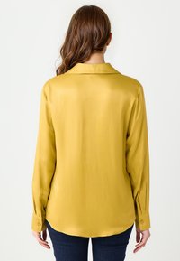 Koszula z długim rękawem w musztardowym satynie z kołnierzykiem, zapinanymi mankietami i okrągłym dołem, widok z tyłu.