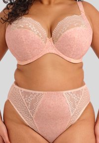 Lichtroze lingerieset met een gevormde beha met kantafwerking en bijpassende hooggesneden slipjes, versierd met bloempatronen en gegolfde randen.