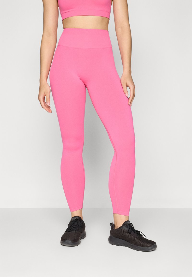 Leggings rosa elasticizzati con vita alta, caratterizzati da una texture liscia e un design aderente. Abbinati a scarpe da ginnastica nere.