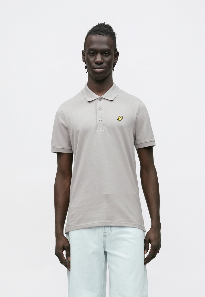 Sivé polokošeľa s logom žltého motýľa na ľavej strane hrudníka, krátkymi rukávmi a trojguľovou légou s hladkou textúrou.