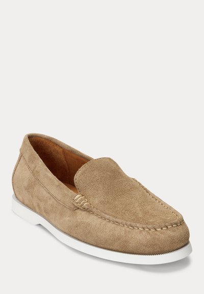 Beige zomšinis loaferis su mokasinų stiliaus nosimi, baltu guminiu padu ir siuvinėjimu aplink viršutinę dalį. Lygus vidinis pamušalas.
