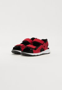 Røde og svarte atletiske sandaler med borrelåsremmer, åpen tå og teksturerte såler; har kontrasterende svarte detaljer og lett design.