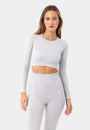 Szary sportowy crop top z długimi rękawami, prążkowana tekstura i małe logo na lewym ramieniu; w zestawie z dopasowanymi leginsami o wysokim stanie.