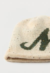 Berretto lavorato a maglia color bianco sporco con macchie multicolori, con una lettera decorativa "A" di colore verde scuro sulla parte anteriore. Tessuto morbido e strutturato.